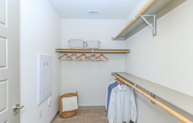 a walk in closet with white walls and shelves and a clothes rack