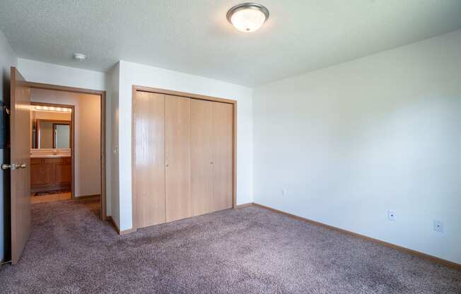 A room with a carpeted floor and a wooden door. Fargo, ND Stonebridge Apartments