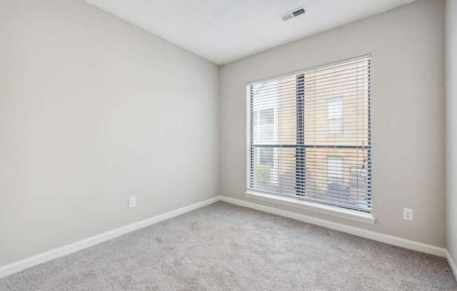 A room with a carpeted floor and a window with blinds.