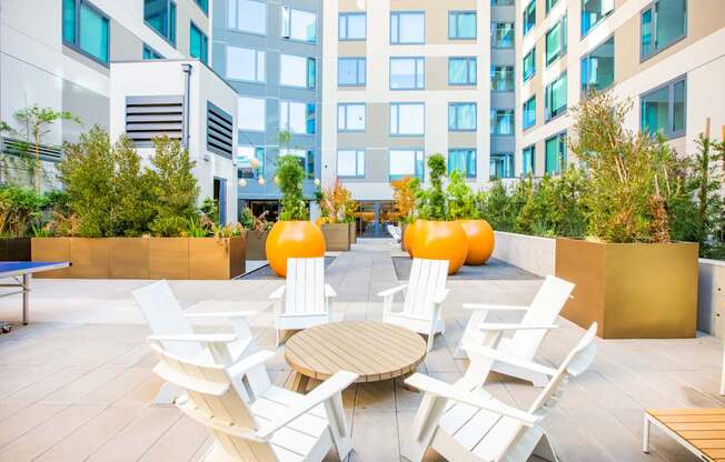 A patio with white chairs and a table surrounded by plants.
