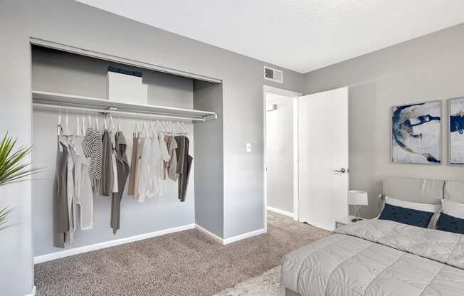 a bedroom with a closet and a bed and a wardrobe with clothes hanging in it
