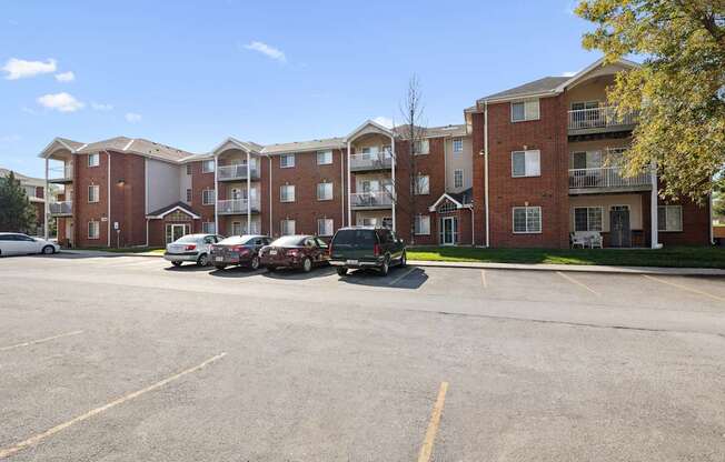 A parking lot in front of a red brick apartment building with cars parked.