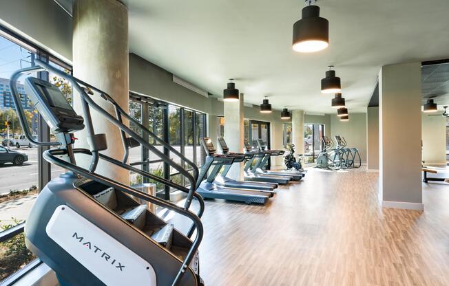 A light-filled fitness area with cardio equipment, expansive windows, and an open layout that supports movement, focus, and everyday wellness.