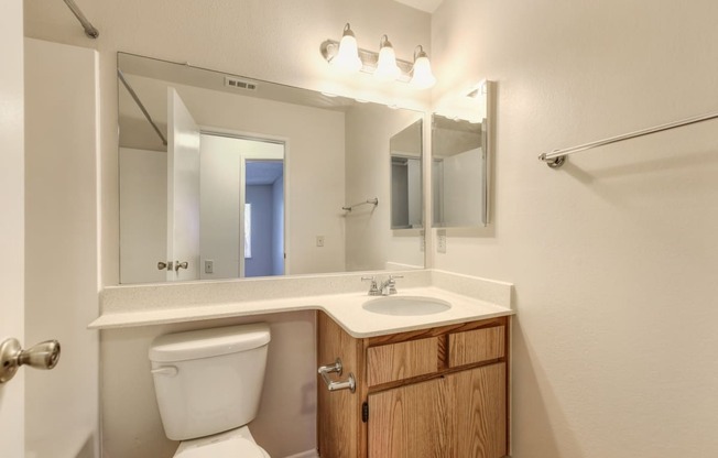 Vacant apartment home bathroom with sink and vanity.  Large mirror and bright lighting above the sink. 