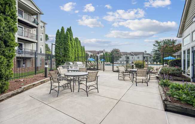 A patio with a table and chairs is surrounded by a fence and has a pool in the background.