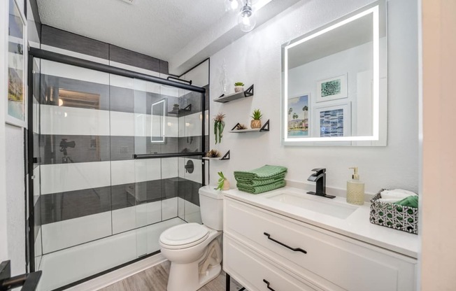 Fusion Warner Center apartments bathroom with black and white tiled shower, lit mirror, and vanity sink with drawer storage.