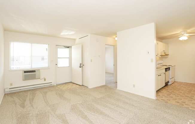 the living room and kitchen of an apartment with white walls and flooring