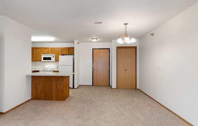 an empty living room with a kitchen and a door to a closet