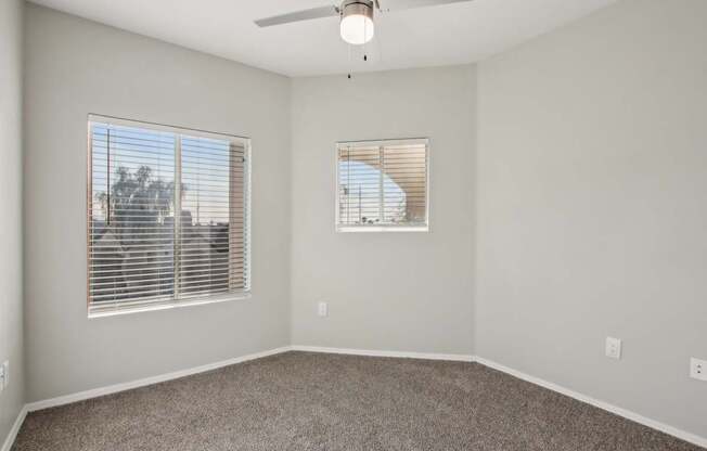 A room with a ceiling fan and two windows.