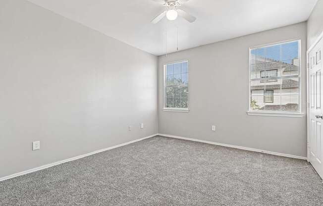 A room with a ceiling fan and two windows.