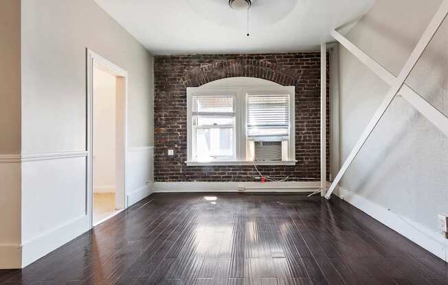 A studio apartment with a brick wall and wooden floors at Brookmore Pasadena apartments.