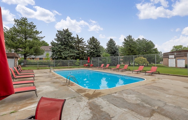 A pool surrounded by red chairs and trees.
