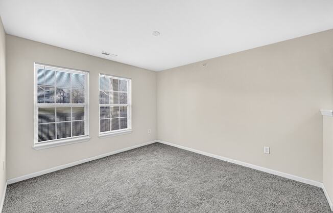 an empty bedroom with two windows and carpeting