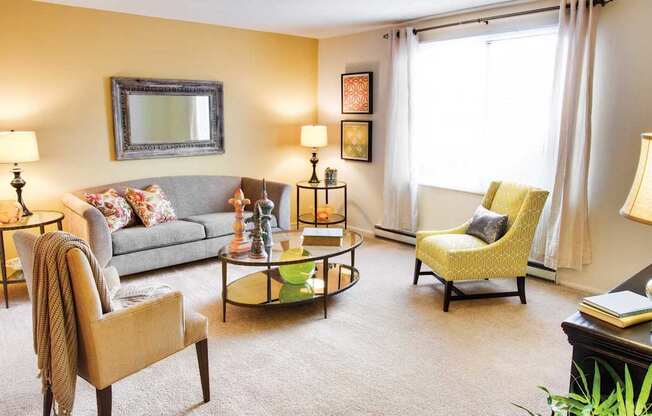 A living room with a grey couch, a yellow chair, and a coffee table at Hummingbird Pointe & The Gardens, Parma, Ohio