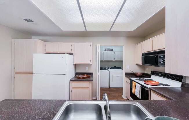 A kitchen with a white fridge and a stainless steel sink.
