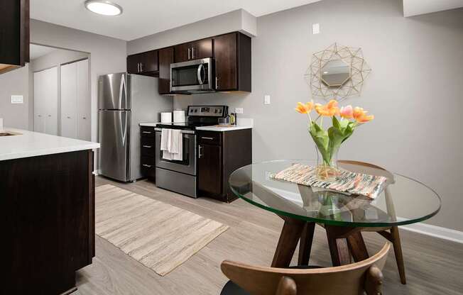 A kitchen with a glass table and a vase of flowers.