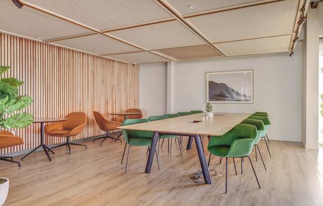 a room with a long wooden table with green chairs and a painting on the wall