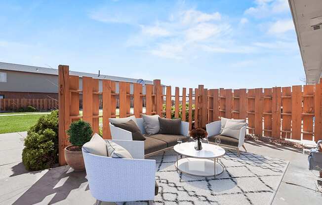 a patio with two couches and a coffee table in front of a wooden fence