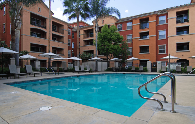 A swimming pool surrounded by apartment buildings and palm trees.