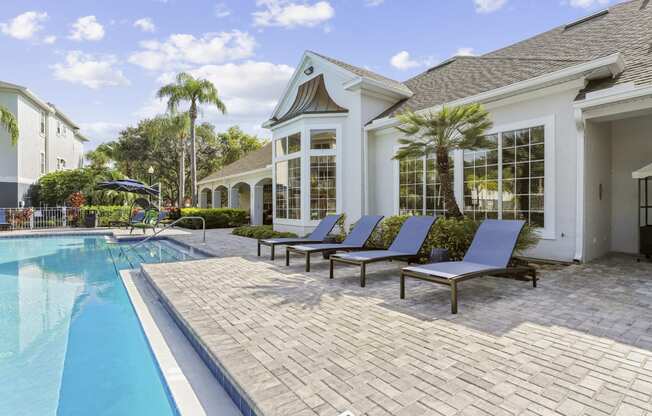 a swimming pool and lounge chairs in front of a house