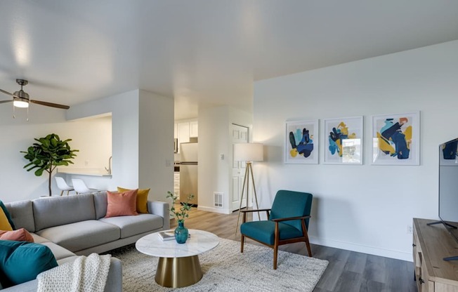 A living room with a grey sofa, a blue chair, a white coffee table, and a painting on the wall.