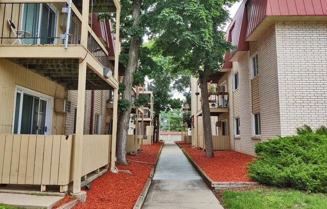 an alley between two buildings with red gravel and trees