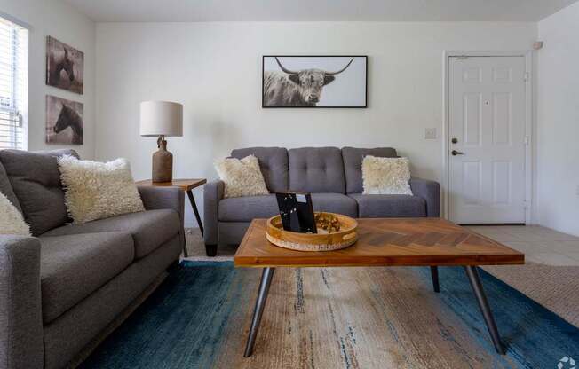 A living room with a grey couch, a wooden coffee table, and a painting of a cow on the wall.