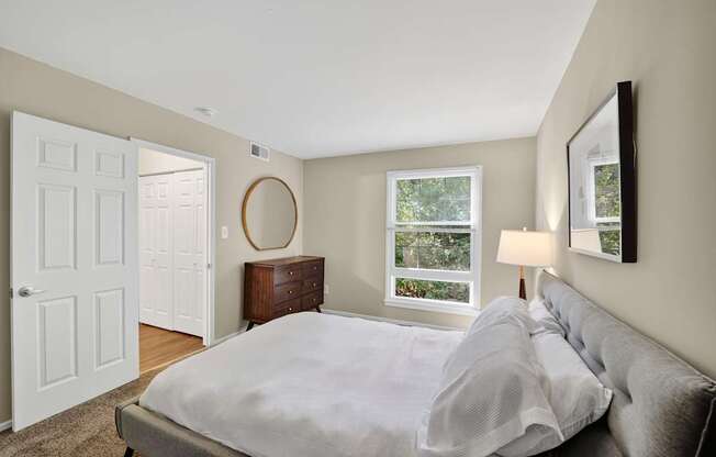 A bedroom with a large bed and a window overlooking a tree-filled yard.
