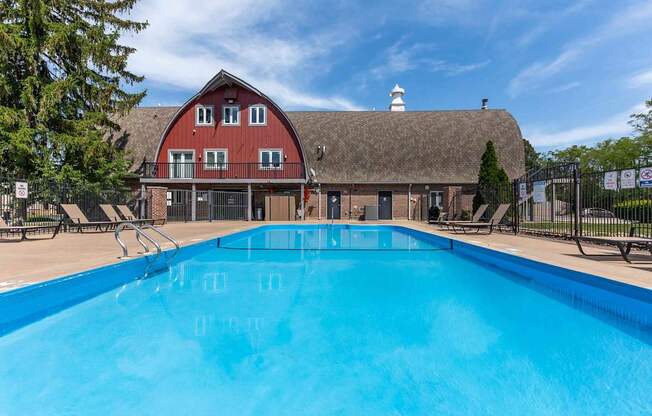 A large blue swimming pool in front of a red barn.