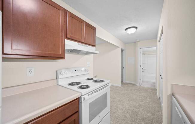 A kitchen with a white stove top oven and wooden cabinets.