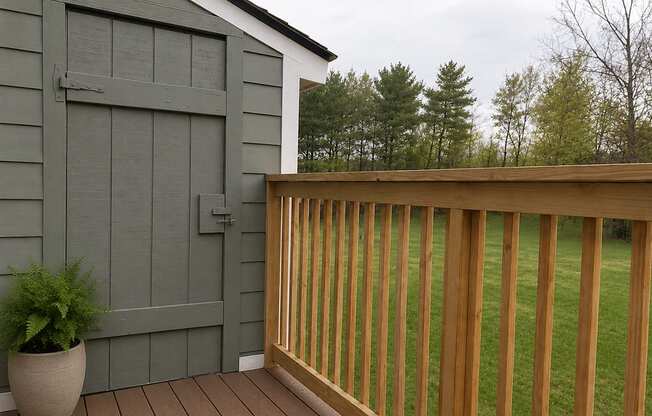 A wooden deck with a grey building and a potted plant.