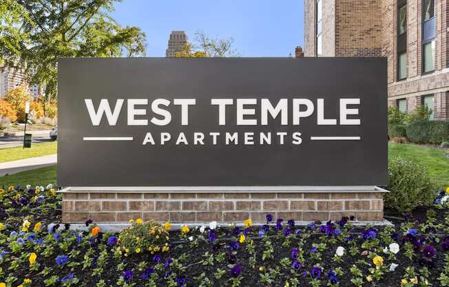 a sign for west temple apartments in front of flowers