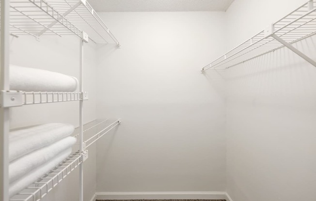 a walk in closet with white walls and shelves and white towels