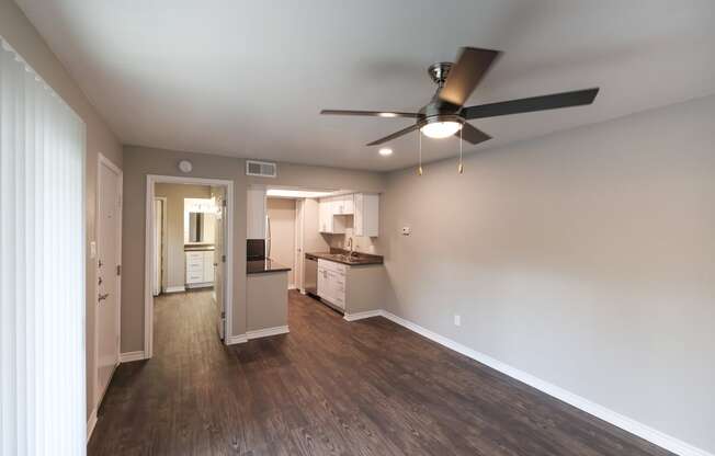 View from living area into kitchen and bedroom. Ceiling fan in living area, whit cabinets and stainless appliances in kitchen