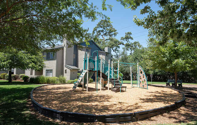 A playground with a green slide and a brown bark dust at Autumn Oaks Apartments, Roseville, CA, 95678