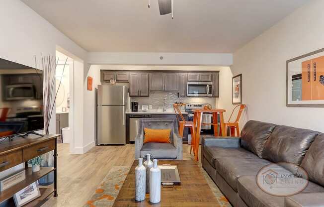 A living room with a leather couch and a kitchen with stainless steel appliances.