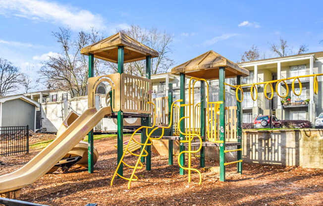 A playground with a yellow slide and a wooden structure.