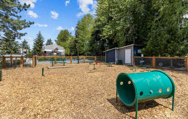 A playground with a green tube slide and a brown wooden fence.