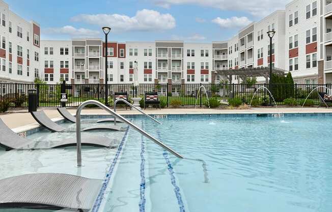A swimming pool with a diving board in front of apartment buildings.