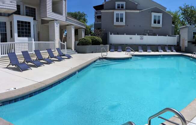 a swimming pool with blue chairs next to a house