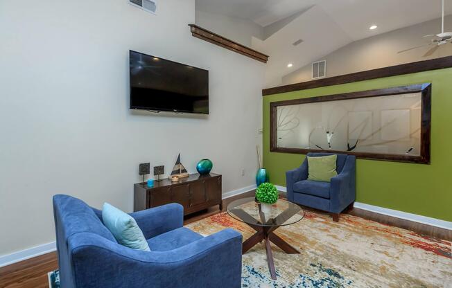 Waiting area with blue chairs and a wall-mounted TV at Ashley Oaks Apartments in Greensboro, NC