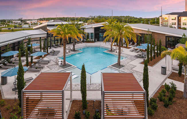 an aerial view of a resort style pool with palm trees and umbrellas