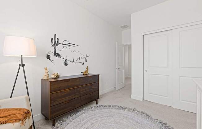 A room with a white door, a brown dresser, and a white lamp.