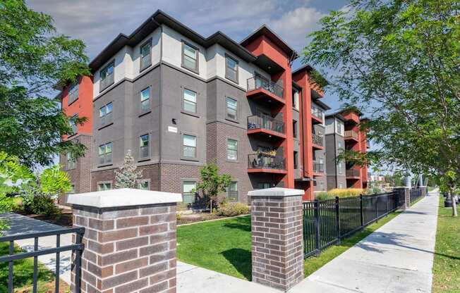 A modern apartment building with a black fence and green trees in the front.