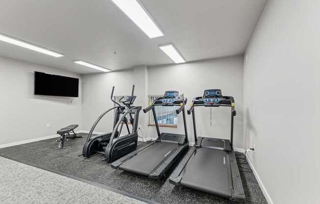 A gym with treadmills, elliptical machines, and a bench.