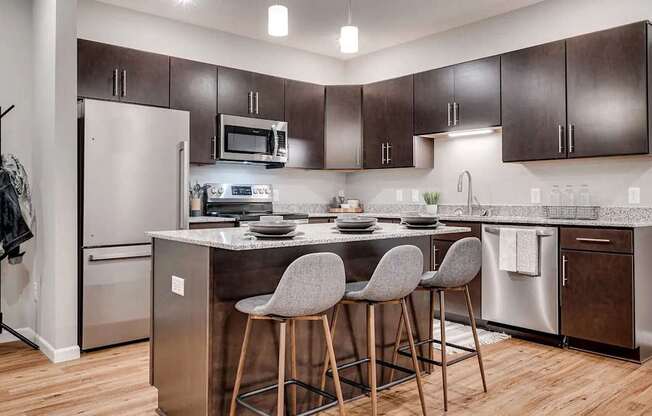 a kitchen with stainless steel appliances and a counter with three bar stools. Circle Pines, MN Lexington Lofts