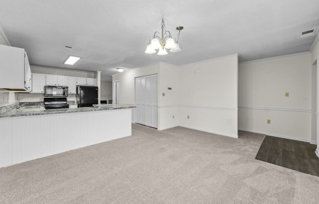 an empty living room and kitchen with white cabinets and a counter top