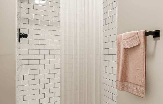 a bathroom with white subway tiles and a shower and a pink towel