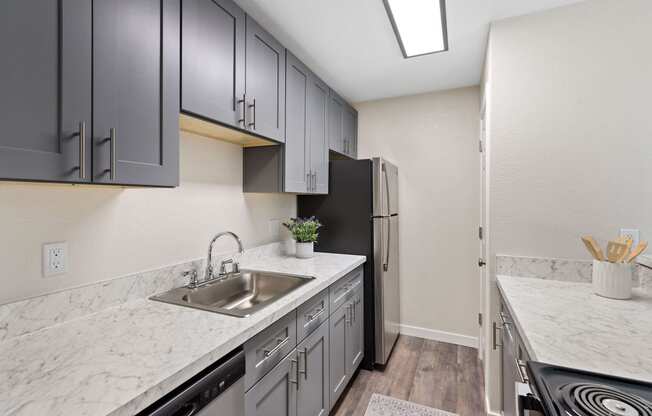 Apartment kitchen with grey overhead cabinetry, plank flooring, and lighting at Hill Crest Apartment Homes, WA 98126