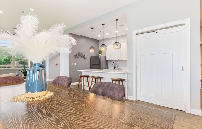 a dining area with a wooden table and chairs and a kitchen in the background